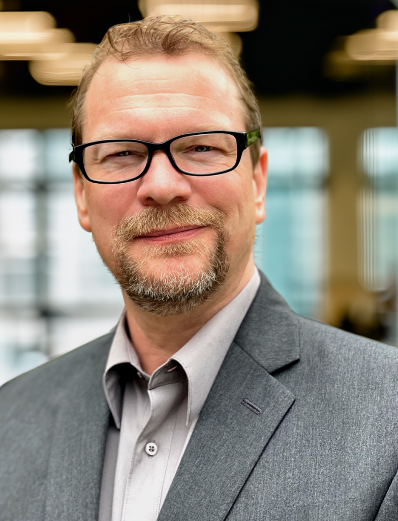 Picture of Jason Aydelott. Middle-aged white man with goatee and glasses wearing a dress shirt and gray suit jacket with no tie.